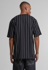 Svart kortärmad t-shirt med vertikala vita ränder. Baksidan har en rundad halsringning och en avslappnad passform.