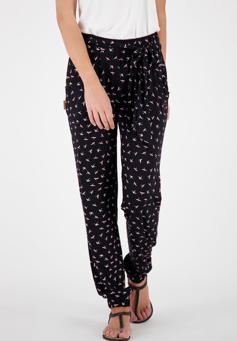 Svarta byxor med dragsko i midjan, prydda med ett mönster av rosa fåglar. Materialet är lätt och har en elastisk mudd. Bärs med platta sandaler.