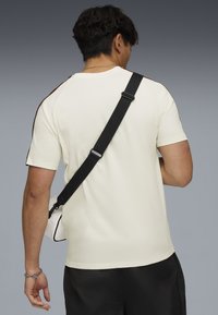 Cămașă scurtă de culoare deschisă, cu dungi întunecate contrastante pe umeri, combinată cu pantaloni scurți negri și o geantă crossbody.