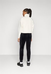 Geknipte witte sweatshirt met hoge kraag, gecombineerd met zwarte fluwelen joggers met elastische boorden en zwarte sneakers. Minimalistisch ontwerp.