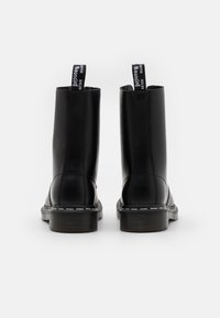 Stivaletti neri alla caviglia in materiale lucido, con punta arrotondata, cuciture a contrasto e linguette con testo sul retro.