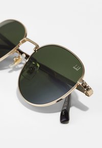 Gold-tone aviator sunglasses with dark green lenses, featuring a double bridge, clear nose pads, and black temple tips with engraved details.