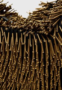 Čierna textilná báza s vyčnievajúcimi kovovými zlatými tyčami, husté usporiadanými, vytvárajúcimi textúrovaný, vrstvený vzhľad.