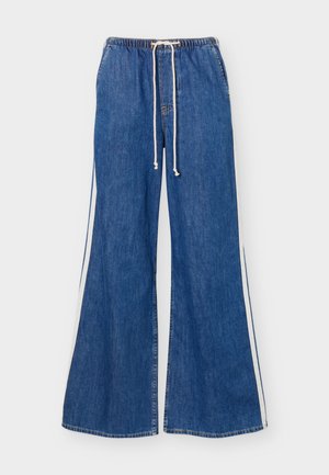 Μπλε τζιν παντελόνι με φαρδιά γραμμή, ελαστική μέση, λευκό κορδόνι και λευκές ρίγες στα πλαϊνά, εμφανίζεται σε λευκό φόντο.