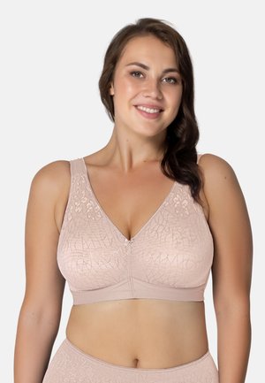 Uśmiechnięta kobieta ubrana w jasnoróżowy, wzorzysty biustonosz bez fiszbin i dopasowaną bieliznę na jednolitym białym tle.