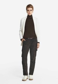 Vit blazer över en brun polotröja, kombinerad med mörka cargobyxor. Sneakers har en vit ovandel och brun sula.