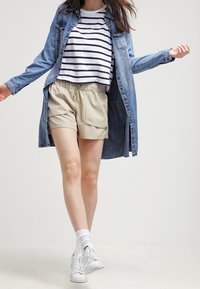Denim shirt coat layered over a white and navy striped crop top, paired with beige shorts, white socks, and white sneakers.
