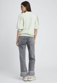 Pull vert clair avec des manches bouffantes, associé à un jean gris taille haute avec un ourlet brut. Des chaussures claires complètent le look.