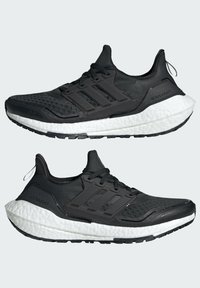 Sorte atletiske sko med en mesh-overdel, tre-stripes branding og en tykk hvid Boost mellemsål. Har teksturerede accenter og en rund tå.