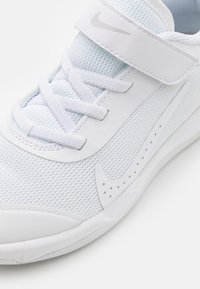 Scarpa sportiva bianca con upper in mesh traspirante, superficie texturizzata e una singola cinturino in Velcro. Presenta un logo argento e accenti perforati.