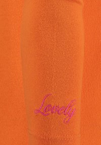 Indumento arancione a maniche lunghe con texture a coste e un'accenno ricamato in rosa "Lovely" sulla manica.