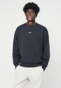 Sweatshirt azul marinho feito de tecido suave, com decote redondo e um pequeno logótipo branco "BOSS" no peito. Ajuste descontraído com punhos canelados.