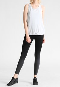 Witte mouwloze sporttanktop gecombineerd met zwarte ombre leggings met een textuurdesign, compleet met zwarte sportschoenen.