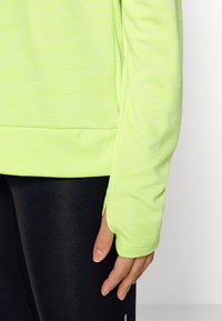 Langärmliges, leuchtend limefarbenes Sportoberteil aus glattem Material, mit Daumenlöchern an den Bündchen und einem leicht geschwungenen Saum.