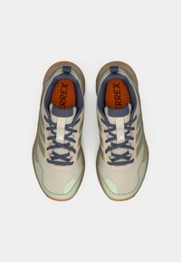 Αθλητικά παπούτσια ανοιχτού χρώματος με πλέγμα και συνθετικά υλικά. Διαθέτουν πράσινες λεπτομέρειες, υφασμένα πέλματα και πορτοκαλί πέλματα.