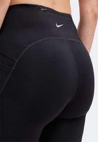 Gros plan sur une personne portant un legging noir taille haute Nike, montrant des coutures détaillées et un petit logo Nike sur la ceinture.
