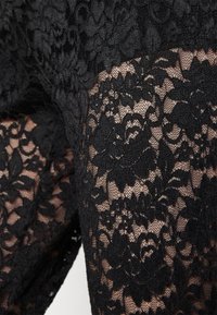 Svart blommig spets tyg med genomskinlig meshbakgrund som visar detaljerade blad- och blommönster.