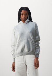 Helehall hall sweatshirt, millel on ees hoiukott, soonikust varrukad ja alläär. Pehme tekstuur ja soe disain, kombineeritud valgete pükstega.