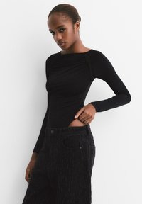 Čierny bodysuit s dlhým rukávom so zhrnutou text�úrou na hrudi, skombinovaný s čiernymi džínami s vysokým pásom, ktoré majú decentné vertikálne vzory.