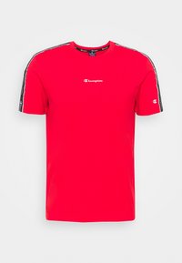 Červené tričko Champion s černou logovou páskou podél ramen a rukávů, malé bílé logo Champion na středu hrudi a na levém rukávu.