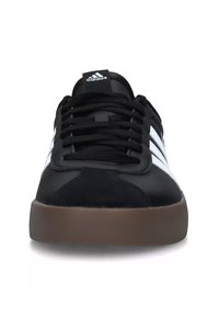 Zapatillas de ante negro con rayas y cordones blancos, que cuentan con una suela de goma marrón y una lengüeta negra grabada con el logo de Adidas.