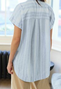 Chemise à manches courtes rayée bleu clair avec un ourlet incurvé et un détail plissé à l'arrière, confectionnée dans un tissu respirant au toucher doux.