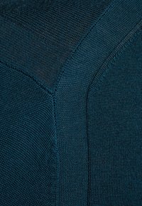 Knitted fabric in deep teal featuring textured patterns and contrasting stitches, showcasing a smooth finish and subtle sheen.