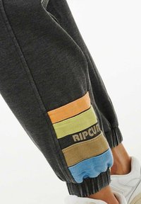 Grå sweatpants med farverige vandrette striber i orange, gul, brun og blå ved bund. Har elastisk talje og ribbede manchetter.