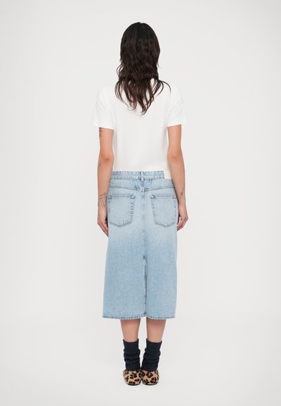 Ανοιχτό μπλε τζιν μίντι φούστα με πίσω τσέπες, λωρίδα μπροστά και ίσια γραμμή. Συνδυασμένη με λευκό μπλουζάκι και παπούτσια με σχέδιο.