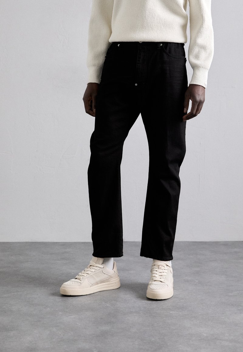 Black denim jeans with a straight cut, paired with cream high-top sneakers and a textured cream sweater. Simple design, no visible patterns.