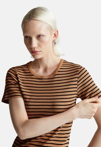 Brązowa i czarna koszulka w paski z okrągłym dekoltem, krótkimi rękawami i miękką fakturą. Charakteryzuje się smukłym krojem.