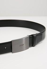 Cinturón de cuero negro con una textura suave y hebilla metálica plateada con el logo "JOOP!". Ajustable con varios agujeros para el tamaño.
