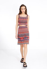 Twee-delig outfit met een crop top en rok in levendige patronen van rood, blauw en turquoise. De stof heeft een gladde textuur, met decoratieve accenten.