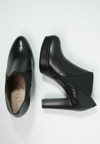 Bottes de cheville noires à talons, en cuir lisse avec un panneau en tissu texturé. Design à talon carré avec un bout rond. Logo discret à l'intérieur.