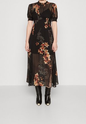 Robe midi noire transparente avec motifs floraux orange, manches bouffantes en dentelle, col montant, associée à des bottines noires à bouts pointus.