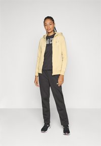 Gelbe Zip-Hoodie, schwarzes T-Shirt mit Print, dunkle Sweatpants und schwarze Sportschuhe. Glatte Texturen und lässiges Design.