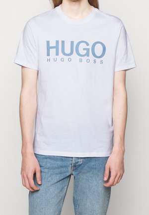 Witte katoenen T-shirt met "HUGO" en "HUGO BOSS" in lichtblauw gedrukt. Korte mouwen en ronde hals. Draagt bij denimjeans.