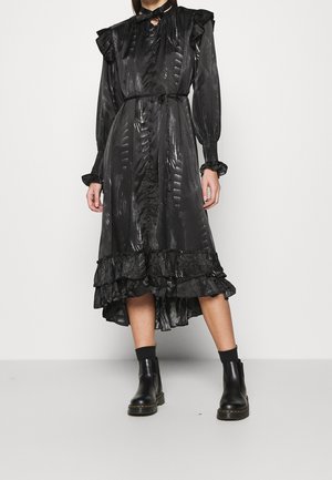 Woman wearing a shiny black midi dress with ruffles, buttons down the front, puffed long sleeves, paired with black ankle boots and socks.