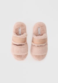 Fuzzy lyserøde skidsandaler med to bløde stropper, der har et logobånd på hver strop. Materialet har en luksuriøs tekstur for komfort.