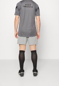 Grå atletisk tröja med "VISIT RWANDA" på ryggen, ihop med ljusgrå shorts och svarta knähöga strumpor. Svarta fotbollsskor fulländar looken.