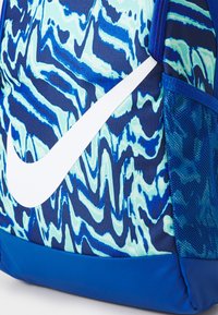 Nike-ryggsäck med ett blått och akvamarinfärgat vågmönster, med en framträdande vit logotyp och ett nätfickor på sidan för ventilation.