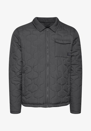 Vaatteena harmaa tilkkutakki, jossa on vetoketjukiinnitys, käännettävä kaulus ja rintatasku. Takki on sileäpintainen ja siinä on pyöreitä kuvioita kankaan pinnalla.