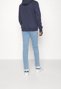 Marinblå huvtröja, ljusblå jeans och vita sneakers med gröna detaljer. Outfiten är avslappnad och åtsittande, vilket framhäver modern stil.