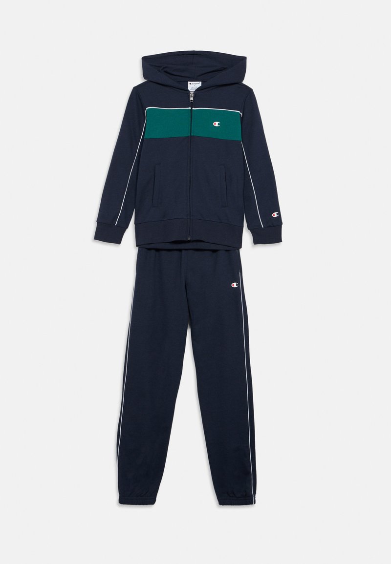 Μπλε σκούρο φούτερ με φερμουάρ και πράσινη ρίγα στο στήθος και αντίστοιχο μπλε σκούρο παντελόνι φόρμας. Και τα δύο έχουν λευκές ραφές και λογότυπα.