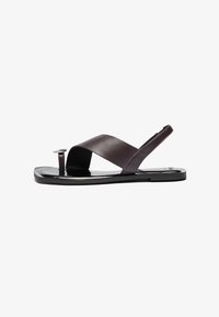Bruna läder-sandaler med en korskorsande remdesign, platt sula och liten cirkulär hårdvarudetalj. Slät textur, minimalistisk stil.