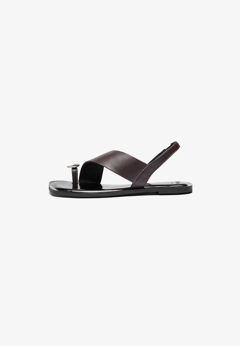 Brown leather sandals with a cross-over strap design, flat sole, and small circular hardware detail. Smooth texture, minimalist style.