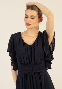 Marineblaues Kleid aus leichtem Stoff, mit kurzen, fließenden Ärmeln, einem V-Ausschnitt und einer gerafften Taille für einen lässigen Sitz.