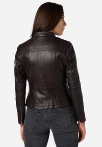 Giacca di pelle marrone con un design aderente, dotata di un alto colletto e polsini con zip, superficie liscia e dettagli di cucitura discreti.