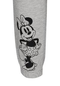 Graue Jogginghosen aus Stoff mit einem schwarzen Grafikdruck eines Cartoon-Charakters mit gepunktetem Kleid und Schleife, deutlich umrissen am Bein.