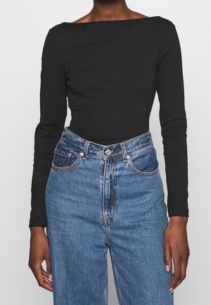 Schwarzes Langarmoberteil mit weitem Ausschnitt, kombiniert mit hoch taillierten blauen Jeans, die eine klassische Denim-Textur und Details der Nähte zeigen.